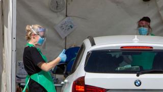 woman in visor and surgical gloves giving thumbs up to person in car