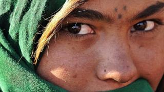 An Afghan girl from a family which returned from Iran covers her face as she stands in front of her tent on the outskirts of Kabul, February 2008