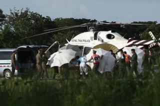 Police and military personnel use umbrellas to cover around a stretcher near a helicopter and an ambulance at a military airport in Chiang Rai