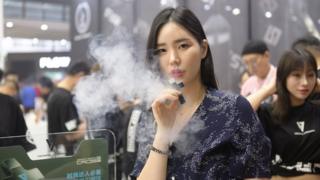 A woman exhales vapor while smoking an electronic cigarette during the 2019 IECIE Shenzhen eCig Expo at Shenzhen Convention and Exhibition Center on April 14, 2019