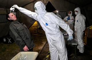 A firefighter wearing a protective suit helps a soldier to take off her face mask