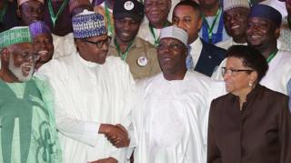 Muhamadu Buhari (hagati i bubamfu) na Atiku Abubakar (hagati i buryo) bahana ukuboko aho bari baje gushira umukono ku masezerano y'amahoro imbere y'amatora, itariki 13/02/2019