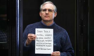 Пол Уилан держит табличку в конце своего судебного процесса: «Фальшивое испытание! Операция с фрикадельками! Никаких прав человека! Жизнь Пола имеет значение!