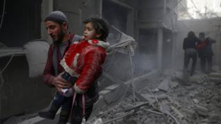 A man holds a child after an air strike in the besieged town of Douma, in the Eastern Ghouta, Syria (7 February 2018)