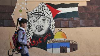 فتاة فلسطينية تمشي إلى جوار جدارية للرئيس الراحل ياسر عرفات