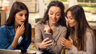 Три женщины в шоке смотрят на экран телефона