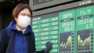 Woman walks past Tokyo stock market board (12/03/2020).