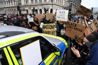 Demonstranten mit Plakaten versammeln sich um ein Polizeiauto
