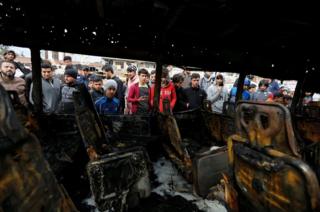 People look at a burned vehicle at the site of car bomb attack in a busy square at Baghdad's sprawling Sadr City district, Iraq