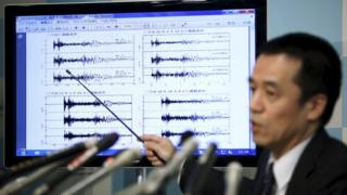 Директор Отдела наблюдений за землетрясениями и цунами Японского метеорологического агентства Йохей Хасэгава указывает на график сейсмических данных