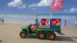 John Deere Gator transformed into ice cream truck selling ice creams to tourists on the beach at seaside resort along the North Sea coast.