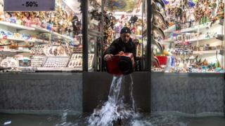 A shopkeeper uses a bucket to remove water from his property in Venice, 13 November 2019