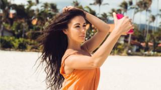 Imagem de uma mulher tirando uma selfie na praia, em pose sensual