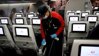 A staff member of Japan Airlines wearing a protective face mask and gloves cleans the cabin of a plane after performing a domestic flight