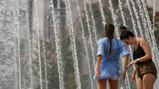 Dos mujeres refrescándose con chorros de agua de una fuente