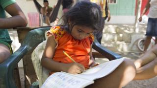 Seven-year-old Shayla Monterlaza, the granddaughter of a displaced woman, studies in front of the community's school with her family