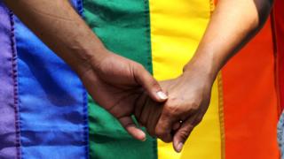 Holding hands in front of rainbow flag