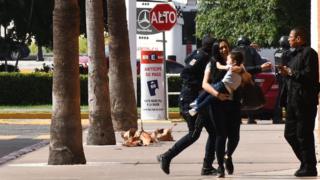 Mujer con chico en brazos y agentes de policía detrás