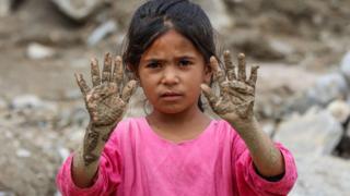 An Afghan girl poses for a photograph after her house was destroyed following heavy floods in Parwan province's Charikar city