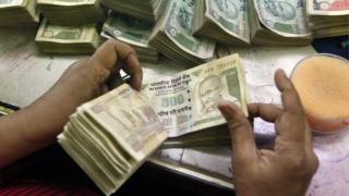 An employee counts Indian currency notes at a cash counter inside a bank