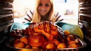 Mulher retira do forno um peru assado com bacon em cima