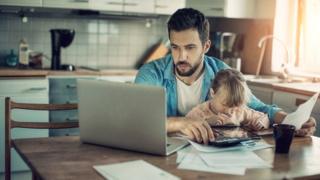 Pai trabalha no computador com a filha no colo
