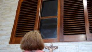 Mujer rezando frente a la ventana en la casa donde se regitró la aparición de la "Santa de la Ventana"