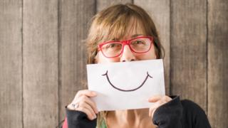 Una mujer sostiene un dibujo de una sonrisa.