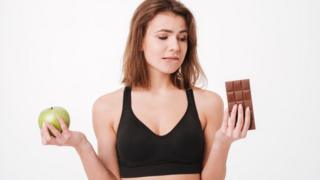 Mujer entre una manzana y una tableta de chocolate.