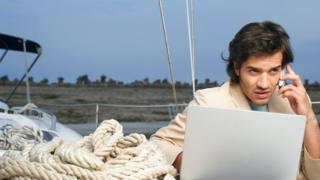 Un hombre que trabaja en su laptop entre cuerdas de navegación (de vacaciones)