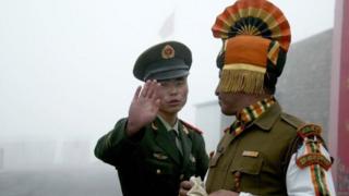 Soldado chinês gesticula enquanto fica perto de um soldado indiano no lado chinês da antiga fronteira de Nathu La entre Índia e China