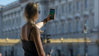 Видно, что женщина играет в Pokemon Go на своем телефоне рядом с Букингемским дворцом в Лондоне
