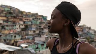 Ckimy, 16, looks out from a rooftop onto the colorfully-painted houses of Jalousie