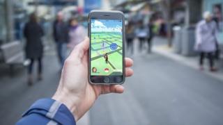 Мужская рука держит iPhone 6 с игрой Pokemon Go на оживленной улице