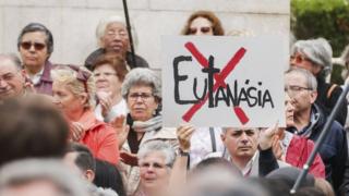 A man holds a sign with a cross struck through the word euthanasia at a demonstration against euthanasia in front of the Portuguese Parliament in Lisbon, Portugal, 29 May 2018