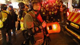 香港九龙旺角一名手持长枪防暴警员在被投掷垃圾桶的警车旁戒备(17/8/2019)