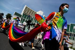 Members of a youth pride student group carry a long piece of rainbow-patterned fabric