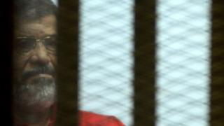 Mohammed Morsi, wearing a red uniform, looks on from behind bars during his trial on espionage charges at a court in Cairo on June 18, 2016.