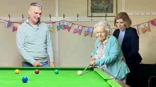 Margaret Cope lining up a shot next to professional snooker player Mark Davis