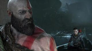 Kratos looks back over his shoulder at his son, sat in a boat behind him.