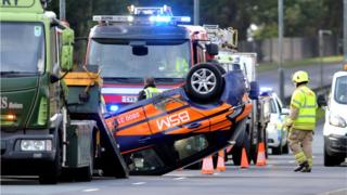 Emergency services at crash scene with one car on its roof
