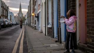 Mädchen schlägt Topfdeckel mit Löffel in Straße