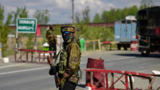 Индийский военнослужащий видел стоящую тревогу, когда конвои индийской армии движутся по Национальному шоссе на окраине Сринагара.