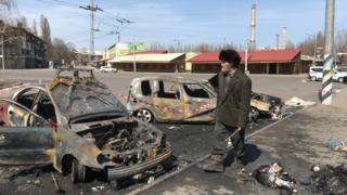 Man walks past burnt cars at site of missile strike