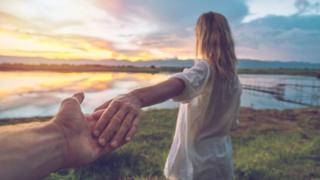 Hombre tomando de la mano a una mujer, que se ve de espaldas.