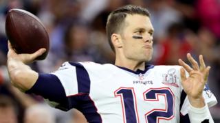 Tom Brady sujeta un balón de fútbol americano.