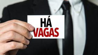 Homem usando terno e gravata segura plaquinha em que se lê "há vagas"