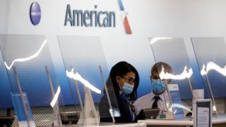 Сотрудники носят защитные маски за пластиковым экраном в зоне регистрации American Airlines в международном аэропорту О'Хара (ORD) в Чикаго, штат Иллинойс