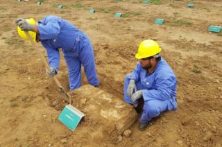 Two men working in blue boiler suits and yellow hard hats to restore graves in Iraq