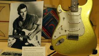 A photo of Dick Dale alongside his custom Fender Stratocaster guitar on display at an exhibit  at the Fullerton Museum Center, California
